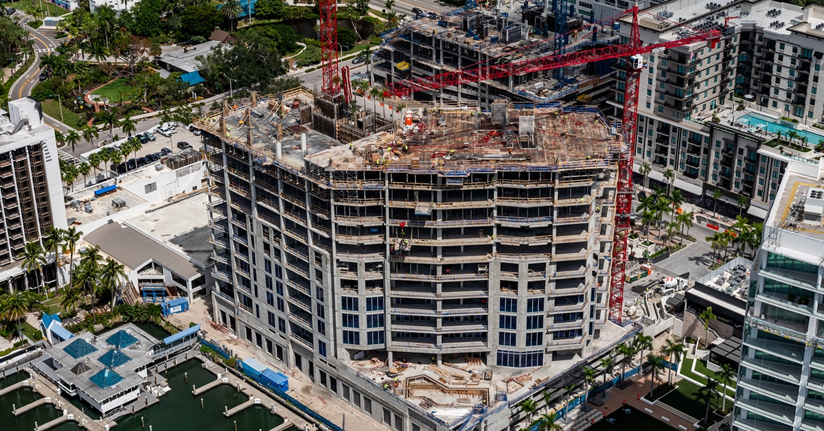 Aerial view of a high-rise residential tower under active construction near the waterfront.