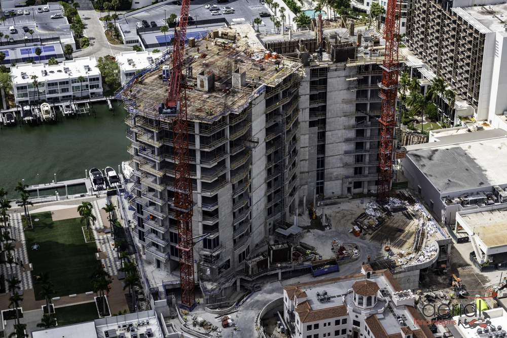 Large waterfront condo building under construction with cranes and marina access in view.