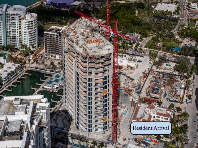 Aerial view of waterfront high-rise under construction with red crane and marina.