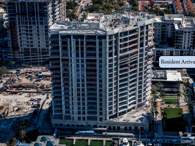 Aerial view of waterfront high-rise under construction beside marina with cranes.
