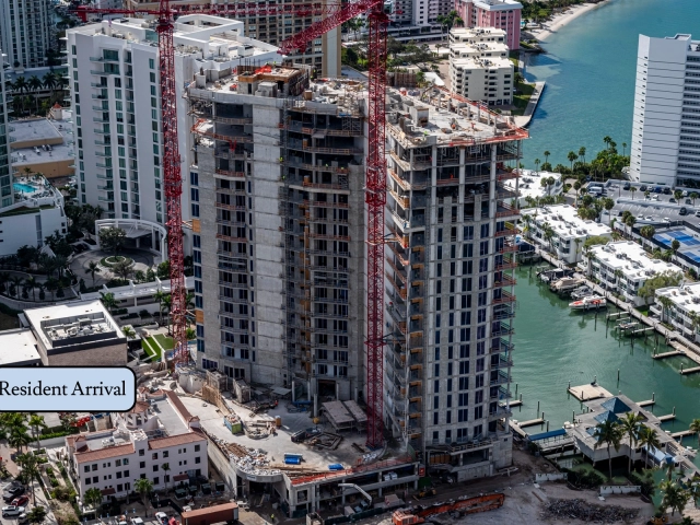 Concrete residential tower under construction with two red cranes near waterway.