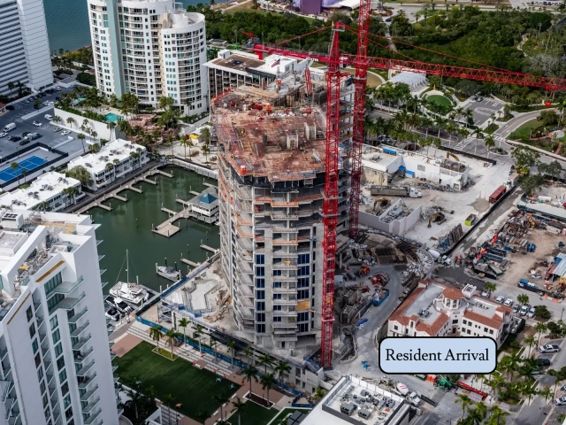 Aerial view of high-rise tower with two red cranes beside marina basin.