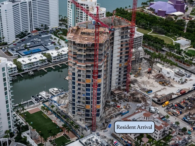 Concrete high-rise under construction with two red cranes near marina basin.