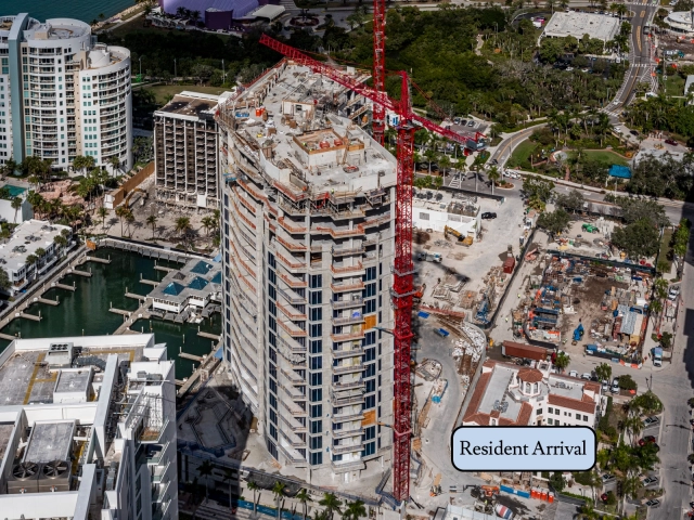 Upper floors of waterfront high-rise during rooftop construction with red crane.
