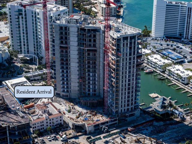 Drone view of waterfront high-rise under construction near marina docks.