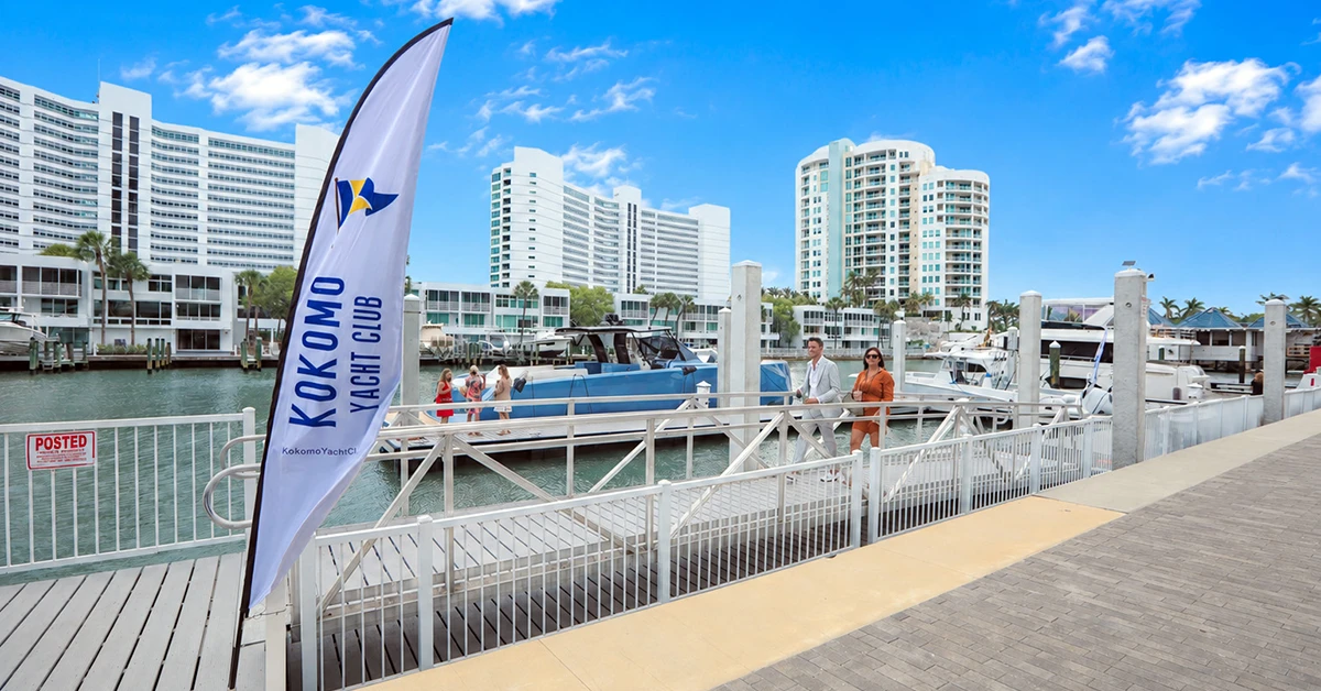 People walking beside marina and yachts near Kokomo Yacht Club flag.