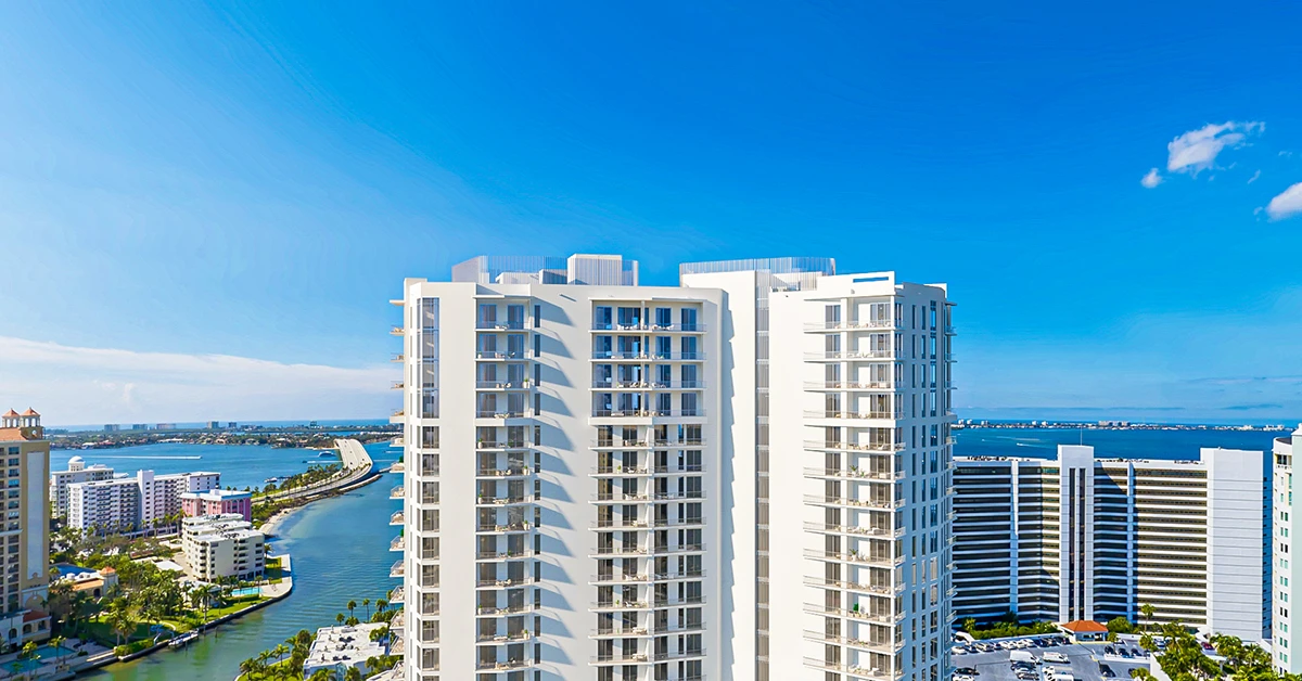White waterfront high-rise residence with balconies beside blue water and nearby towers.
