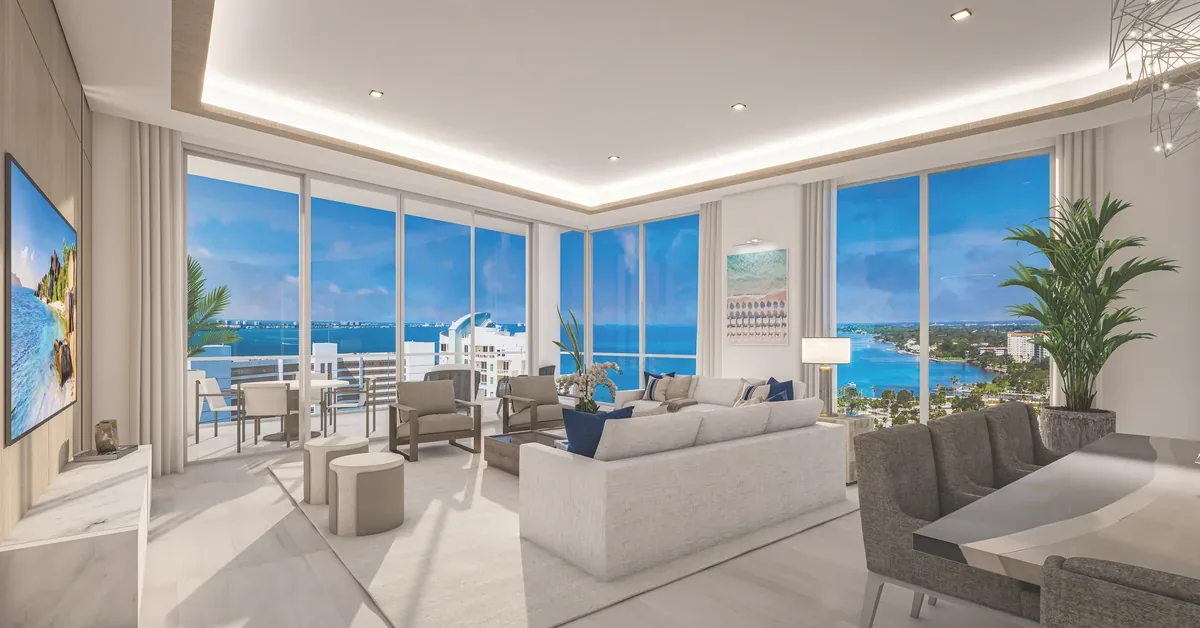 Luxury oceanfront condo living room with floor-to-ceiling windows, modern furnishings, and panoramic turquoise water views from a high-rise balcony.