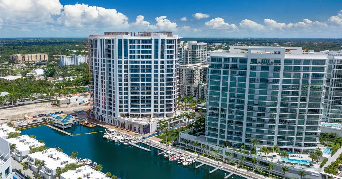 Aerial view of modern luxury waterfront condominiums with private marina, palm-lined promenades, and resort-style amenities along a Florida coastal community.